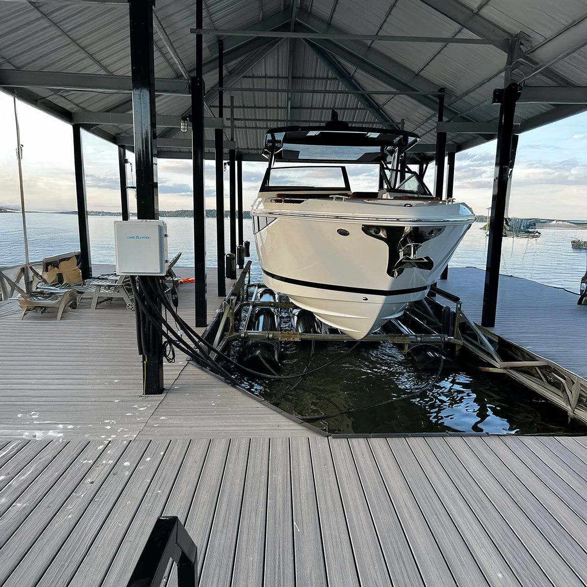White boat docked under a wooden pier with a view of water and sky.