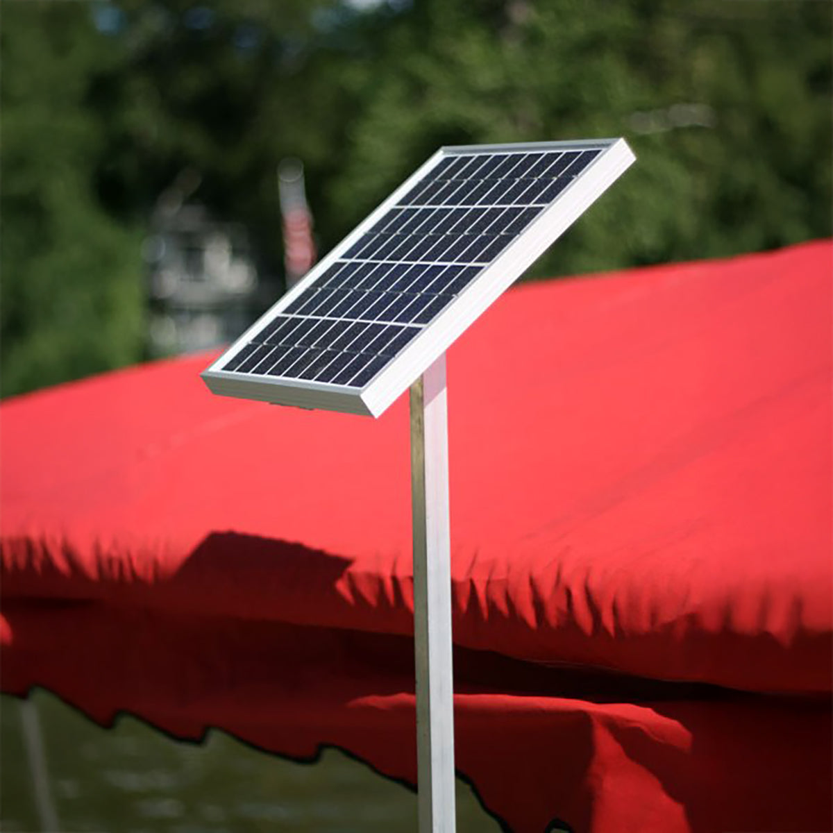 Solar panel on a stand in front of a red awning with greenery in the background