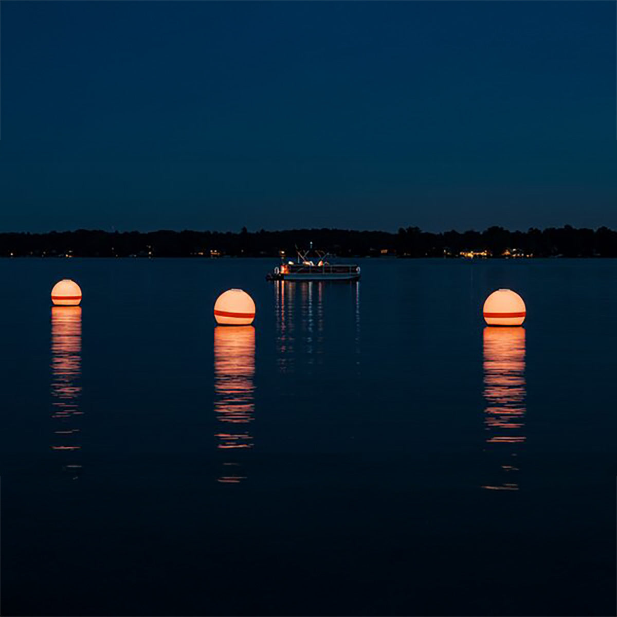 Three illuminated spherical lights on a body of water at night with a boat in the background.