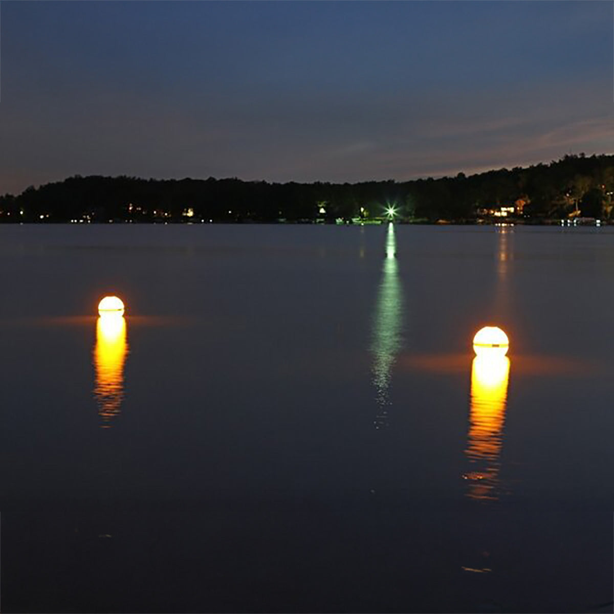 Two illuminated buoys on a calm lake at night with trees in the background.