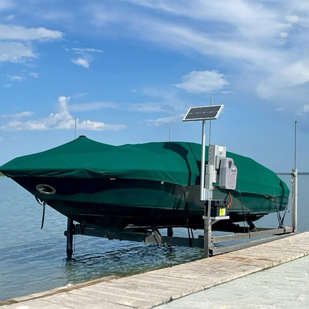 Boat on a lift with a green cover and solar panel on a dock under a blue sky.